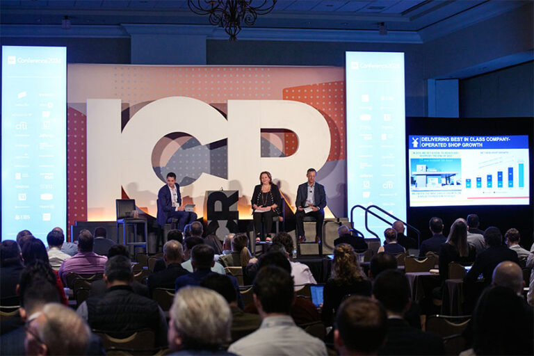 Three people speaking on stage with crowd of people